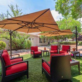 A cozy outdoor patio setup with red cushioned chairs and large umbrellas surrounded by greenery.
