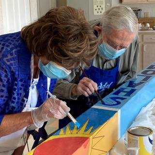 Two people wearing masks engage in a collaborative painting project.