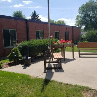 A sunny outdoor area featuring benches and lush greenery near a building.