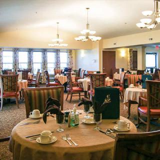 An empty restaurant dining room with set tables and chairs, featuring chandeliers.