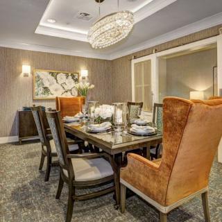 A modern dining room with a large chandelier, elegantly set table, and orange chairs.