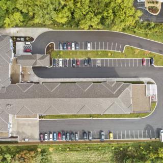 An aerial view of a building with a surrounding parking lot and driveway, bordered by trees.