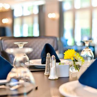 A beautifully set dining table in a restaurant with elegant glassware, folded napkins, and a small flower arrangement.