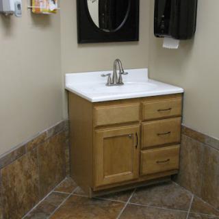 A corner bathroom sink with wooden cabinetry and a mirror above it.