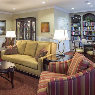 A cozy living room with a sofa, armchairs, bookshelves, and decorative lamps.