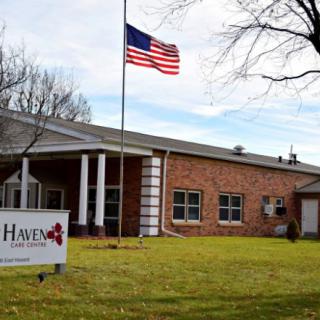 A brick building with an American flag, a sign on the lawn, and trees in the background.