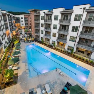 Aerial view of a modern apartment complex featuring an illuminated outdoor swimming pool in the evening.