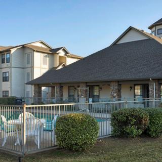 A residential apartment complex with a pool surrounded by a fence and landscaping.