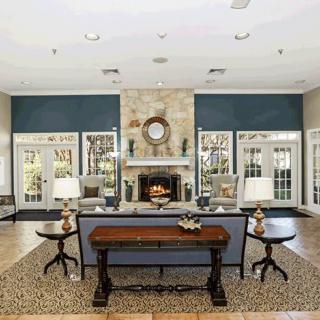 A spacious living room featuring a central fireplace, surrounded by elegant furniture and ample natural light from large windows.