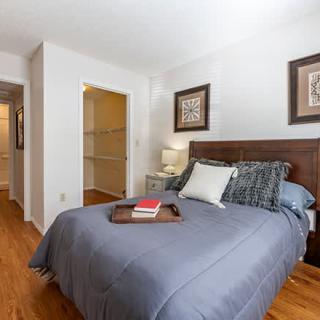 A cozy bedroom with a neatly made bed, wooden floor, and decorative wall art.