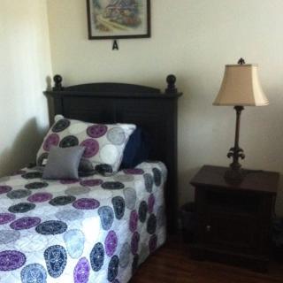 A cozy bedroom with a single bed decorated with a colorful quilt, beside a wooden nightstand and lamp.