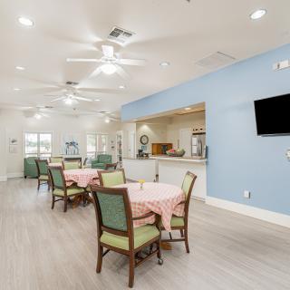 A spacious dining area with tables and chairs, featuring ceiling fans and a television mounted on the wall.