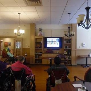 Residents in a nursing home gather to watch television together in a common area.