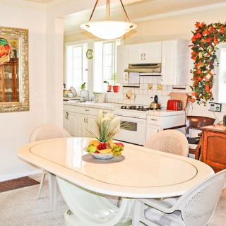 A cozy kitchen and dining area featuring a table with a fruit bowl, surrounded by chairs and decorated with greenery.