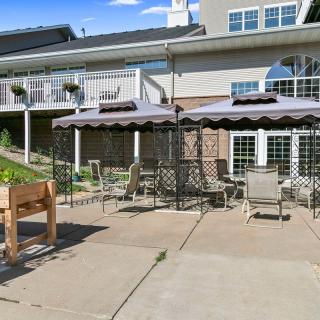 Sunny patio area with outdoor furniture and umbrellas in front of a building.