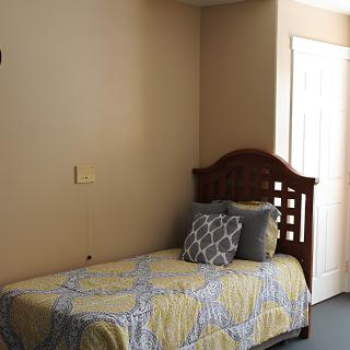 A simple bedroom featuring a single bed with a wooden headboard, adorned with patterned bedding and pillows.