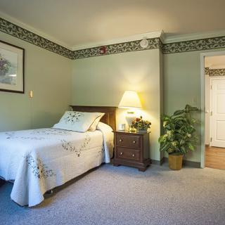 A cozy bedroom with a single bed, a nightstand with a lamp, and decorative trim on green walls.