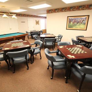 A spacious game room featuring several tables with chess boards and a pool table in the background.