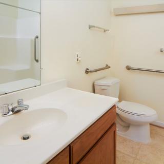 An accessible bathroom with a sink, toilet, and handrails.