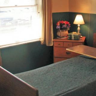 A cozy bedroom with a single bed, a small lamp on the bedside table, and a window letting in natural light.