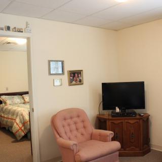 A cozy living room with an armchair and a television, opening up to a bedroom.