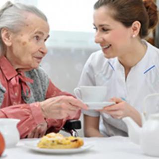 An elderly woman having tea and conversation with a caregiver.
