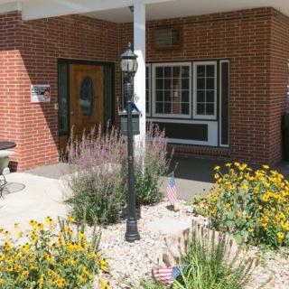 The entrance of a brick building with a garden featuring yellow flowers and a lamp post.
