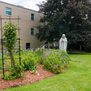 A serene garden with a statue surrounded by greenery and flowers in front of a building.