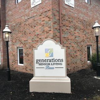 A sign for Generations Senior Living in front of a brick building with lamp posts.