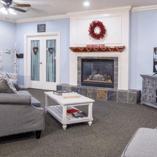 A cozy living room featuring a fireplace adorned with a red wreath, comfortable gray sofas, and a white coffee table.