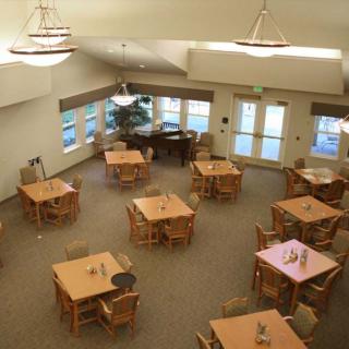 A spacious dining area with multiple tables and chairs, featuring a piano and large windows.