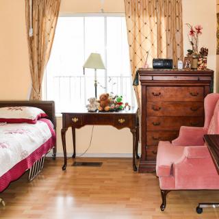 A cozy bedroom with wooden furniture, including a bed, chest of drawers, and armchair by the window.