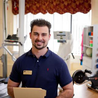 A fitness trainer smiling while holding documents in a gym setting.
