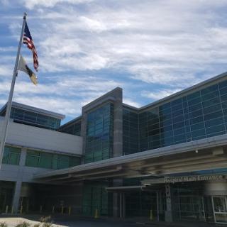 A modern hospital building featuring a glass facade and an American flag waving in front.