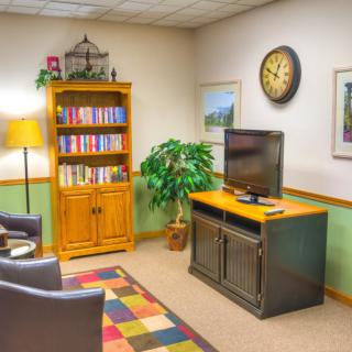 A cozy waiting room with a television, bookshelf, and comfortable seating.
