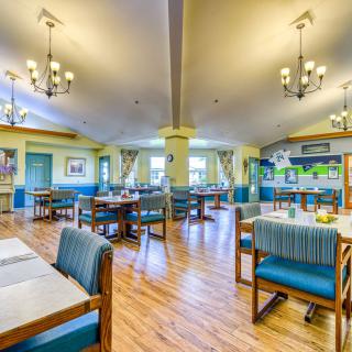 A well-lit and inviting dining area with arranged tables and chairs, featuring chandeliers and a wooden floor.