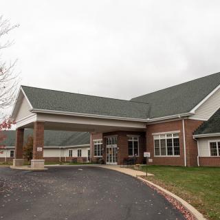 A brick building with a green roof and a driveway leading to the entrance on an overcast day.