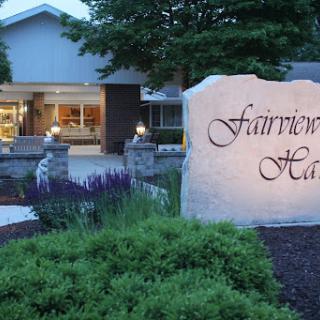 Entrance of Fairview Hall during the evening, featuring a beautifully lit sign amidst lush landscaping.