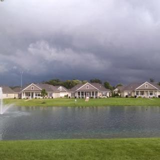 A tranquil neighborhood scene with houses beside a pond, set against a dramatic stormy sky.