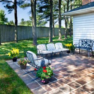 A cozy backyard patio with comfortable seating and vibrant potted plants surrounded by tall trees.