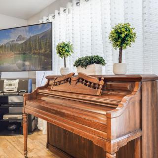 A cozy living room with a classic wooden piano, decorated with potted plants and a television.