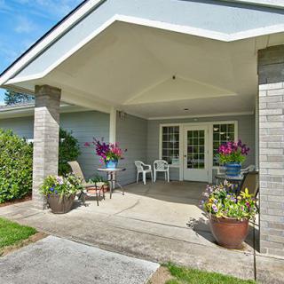 A cozy porch with outdoor seating and vibrant flower arrangements, leading to the entrance of a house.