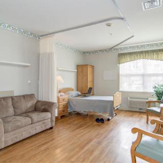 A well-lit patient room in a hospital featuring a bed, sofa, and seating area.