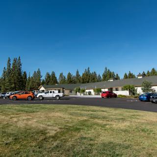 A view of a building surrounded by a parking lot filled with cars, set against a backdrop of trees and a clear blue sky.