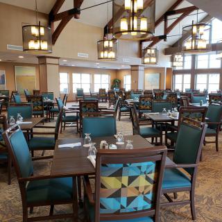An elegant dining area with neatly arranged tables and chairs, illuminated by chandeliers in a spacious setting.