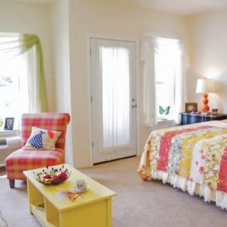 A cozy and colorful bedroom with a vibrant bedspread, a comfy chair by the window, and a small coffee table.