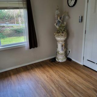 A room with hardwood flooring, featuring a window, a decorative plant stand, and a wall clock.