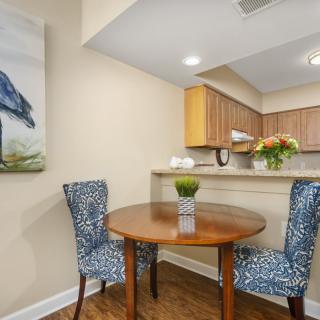 Cozy dining area with a round wooden table and patterned chairs, adjacent to a kitchen.