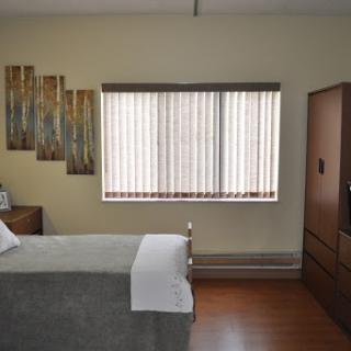 A cozy bedroom featuring a neatly made bed, wooden furniture, and a window adorned with blinds.