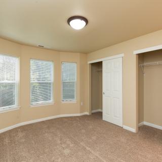 An empty bedroom with carpet flooring, a light fixture on the ceiling, and windows with blinds.
